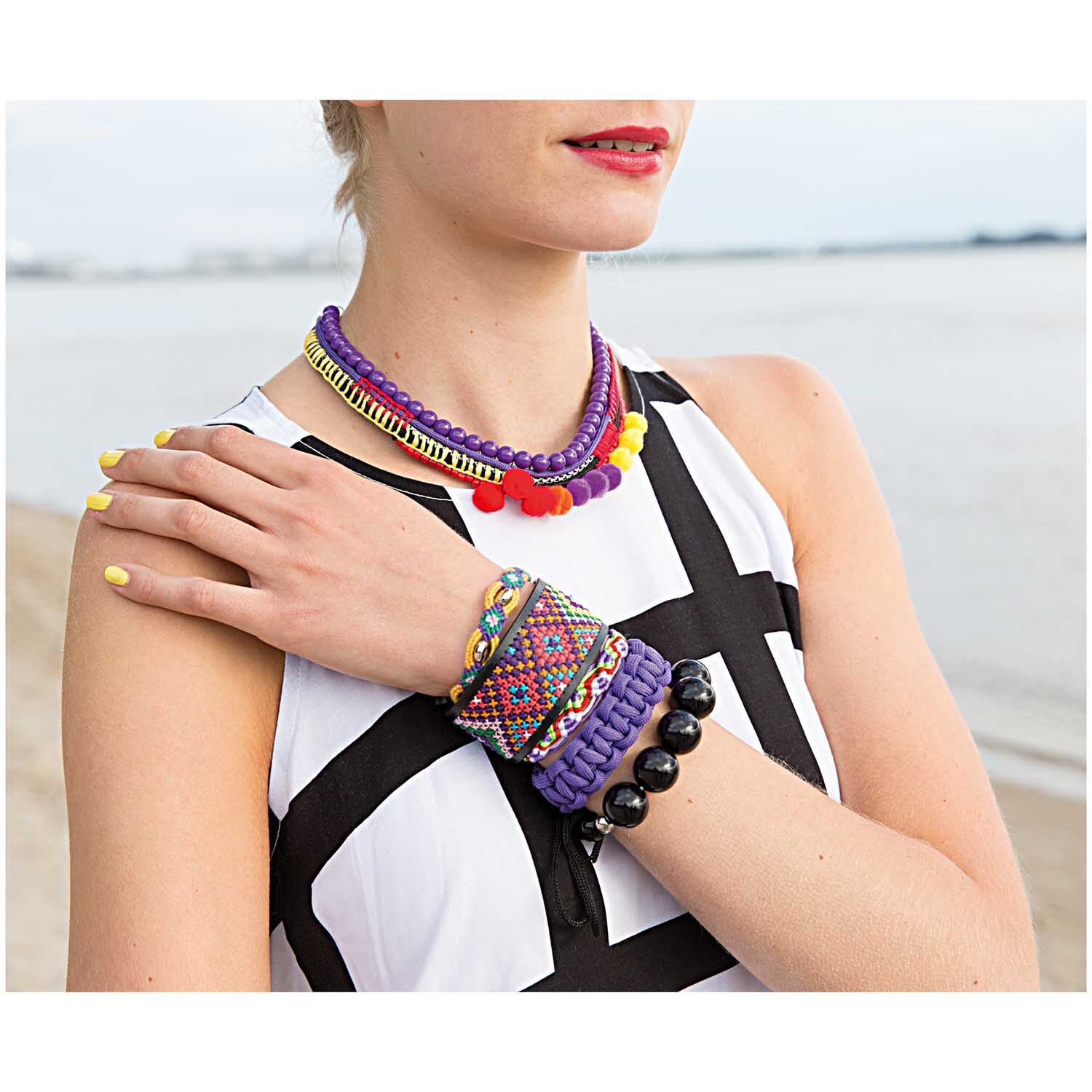 Acrylkugel 16mm 6 Stück: Frau trägt lila Halskette und Armbänder von Rico Design am Strand.