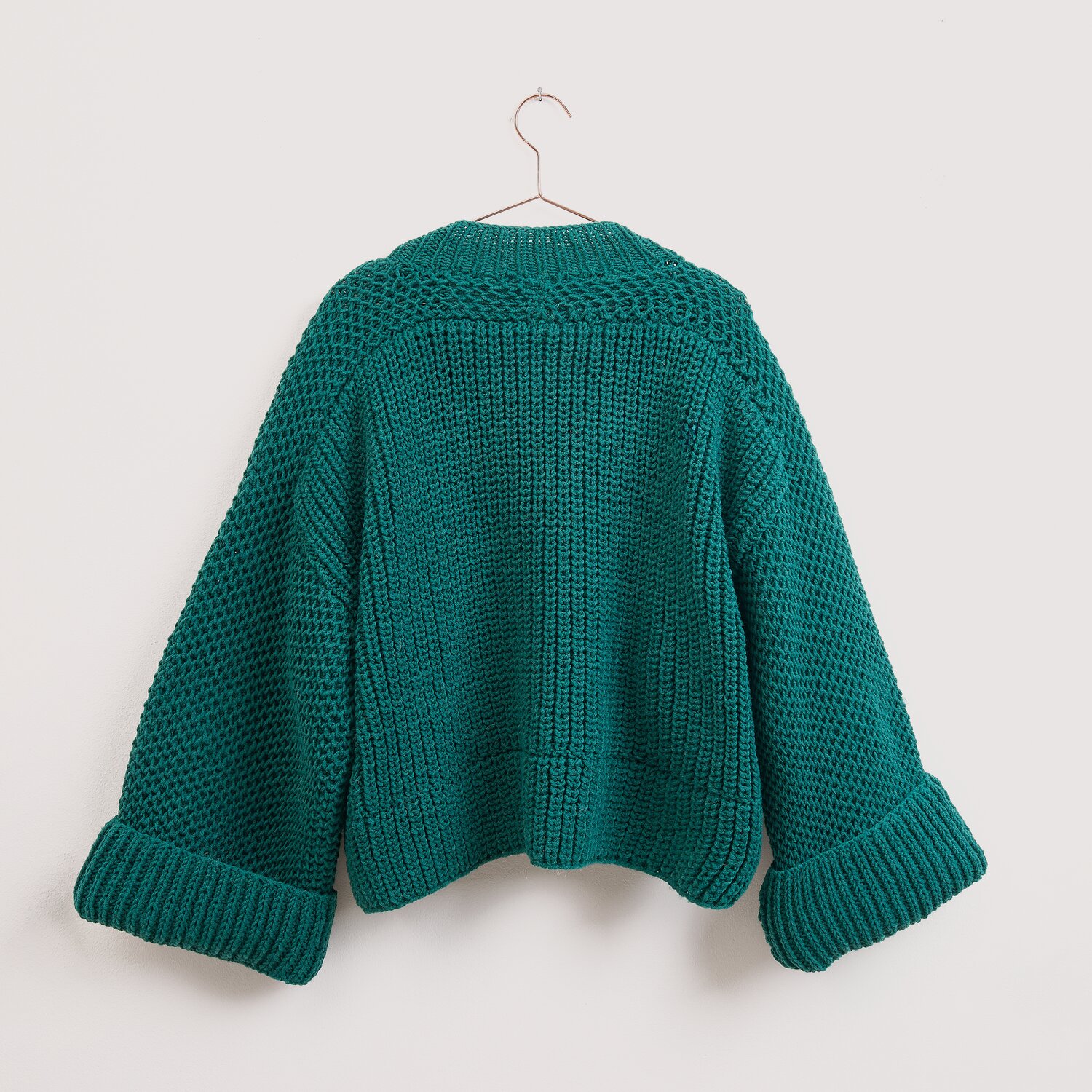 Die Neue Masche No. 16 Herbst Strickjacke von Wolle Rödel, locker geschnitten mit breiten Bündchenärmeln, rückseitig auf Bügel vor heller Wand hängend