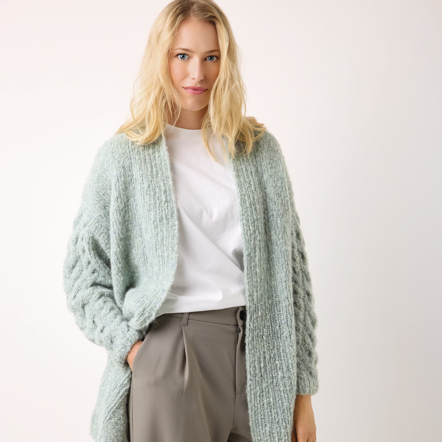 Strickset Jacke Modell 25 aus Die Neue Masche No. 13 von idee. Creativmarkt Strickset Jacke Modell 25: Frau trägt mintgrüne Strickjacke über weißem Shirt und grauer Hose.