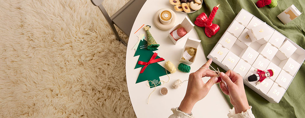 Ricorumi Adventskalender auf Tisch Ricorumi Adventskalender liegt geöffnet auf einem Tisch und Person häkelt.