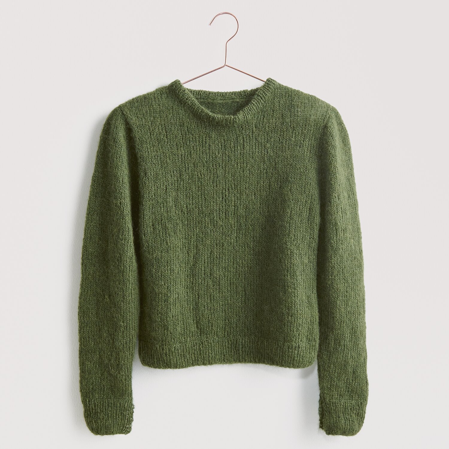 Strickset Pullover Modell 21 aus Luxury Knits: Grüner Pullover aus natürlichen Fasern, hängend an einem Kleiderbügel vor grauem Hintergrund.