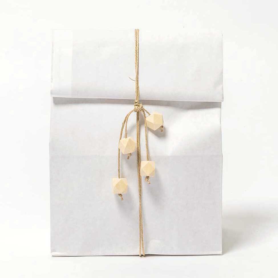 Holzperlen Diamant 3x2x2cm 3 Stück: Naturfarbene Perlen von Rico Design an weißer Papiertüte befestigt.