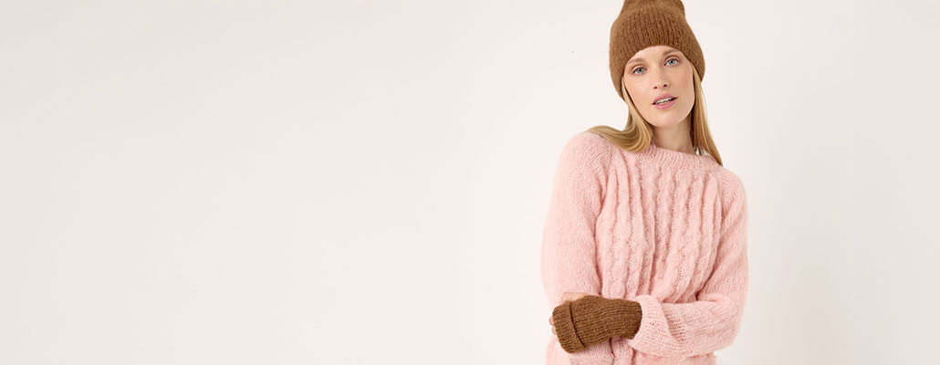 Frau trägt rosa Pullover, Stulpen und Mütze - alles gestrickt