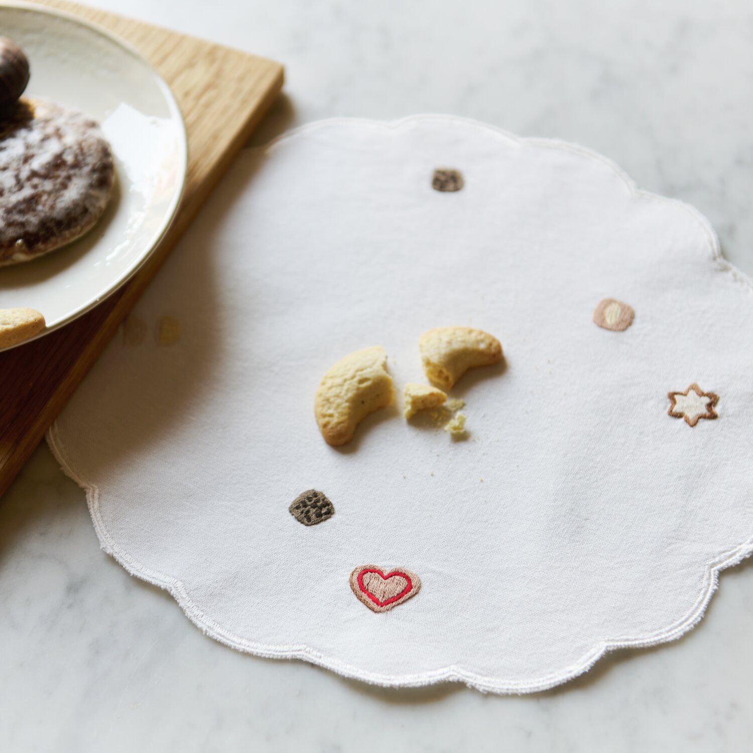 Platzsets rund Weiß 2 Stück, Ø30cm, mit gestickten Keksmotiven auf weißem Stoff, dekorativ auf einem Tisch arrangiert.