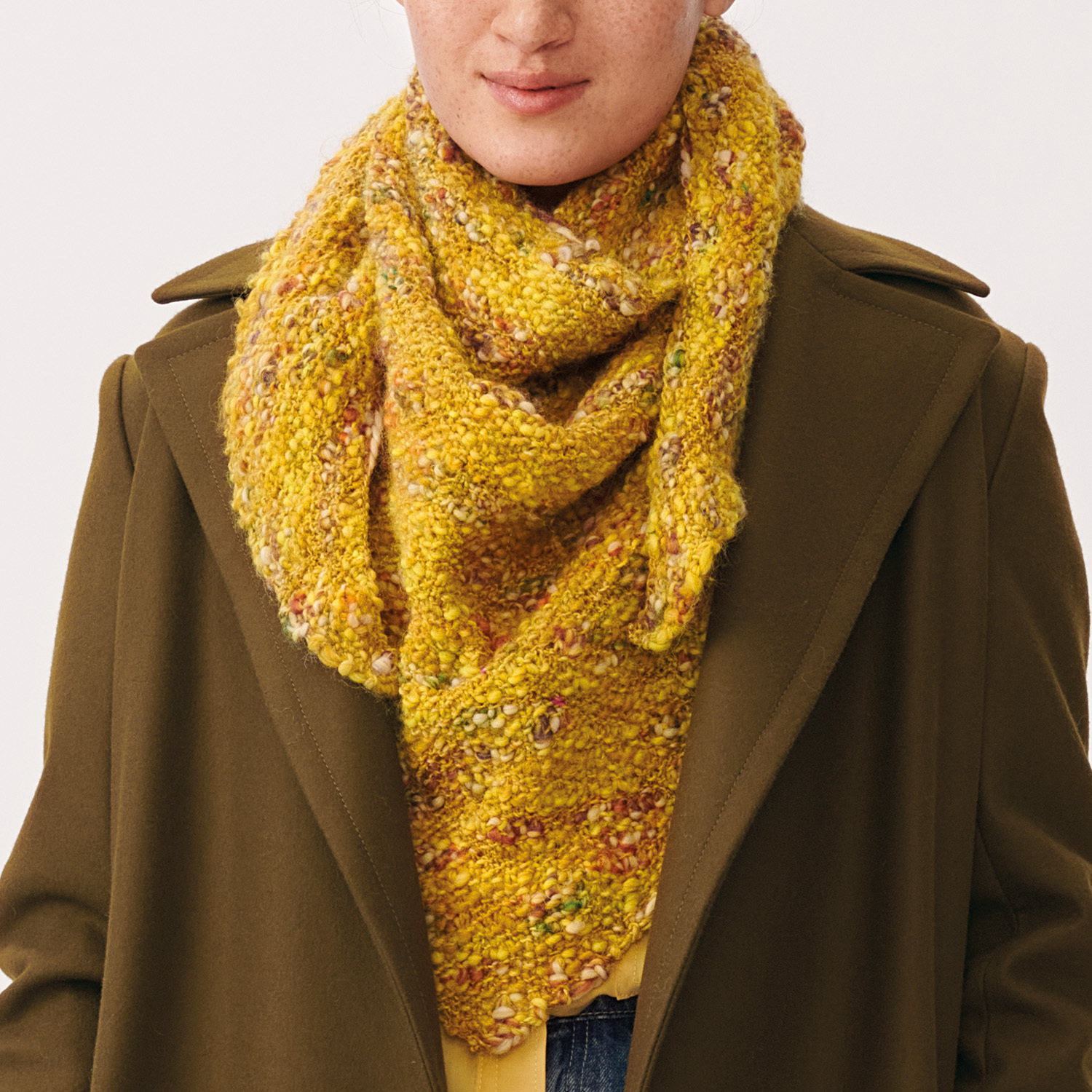 Strickanleitung Tuch aus Creative Wooly Waves: Gelbes, gestricktes Tuch, getragen über braunem Mantel. Ideal für kühle Tage.