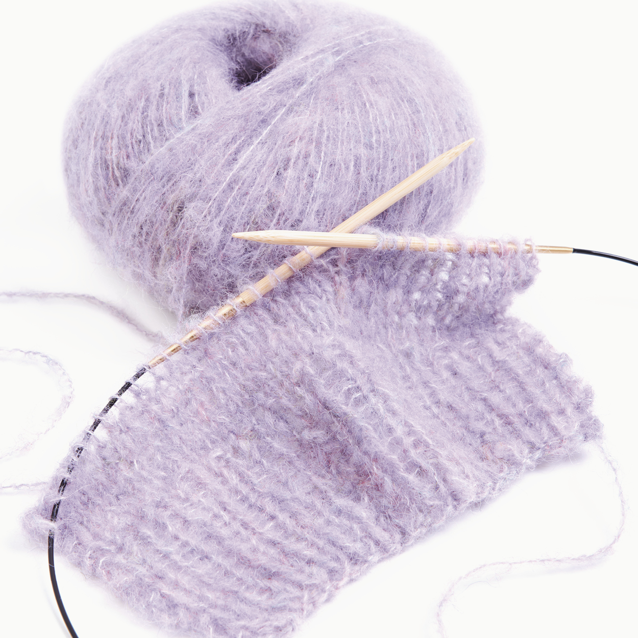 Lila Wollknäuel mit Rundstricknadeln und Strickstück. Flatlay von Produkten.