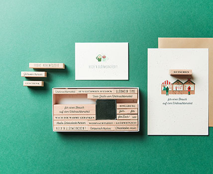 Zwei Karten mit weihnachtlichen Motiven und weihnachtlichen Schriftzügen verziert, daneben ein Stempelset mit festlichen Sprüchen. Flatlay von Produkten.