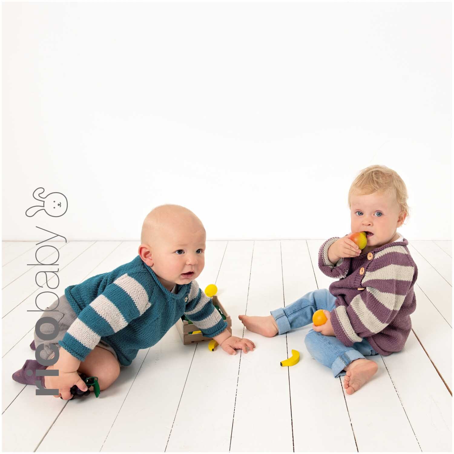 Rico Baby Cotton Soft dk: Zwei Babys in gestrickten Pullovern spielen auf einem weißen Holzboden.