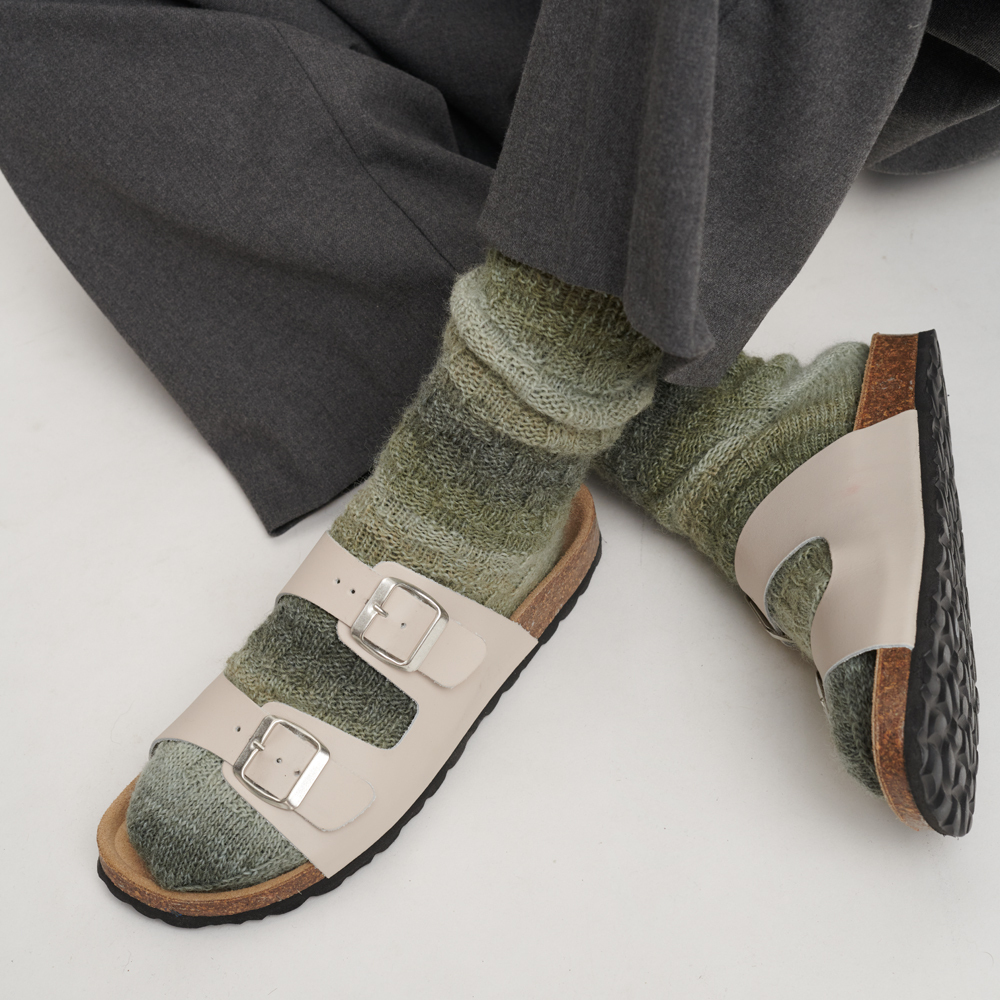 Strumpfwolle Color: Person trägt olivfarbene Socken aus Wolle Rödel, kombiniert mit Sandalen auf weißem Hintergrund.