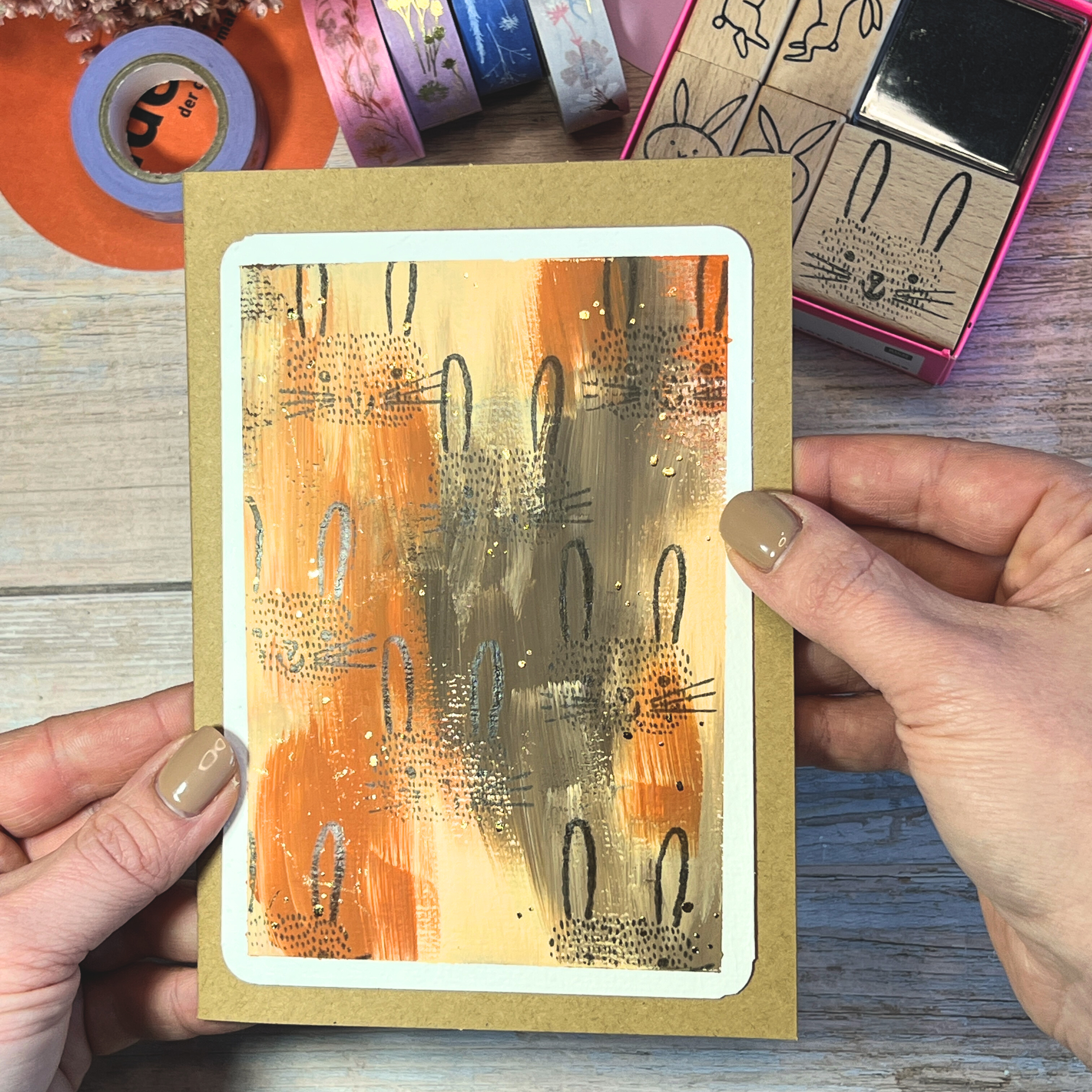 Eine Karte mit schwarzen Hasenköpfen auf braun geflecktem Hintergrund, wird in Händen gehalten.