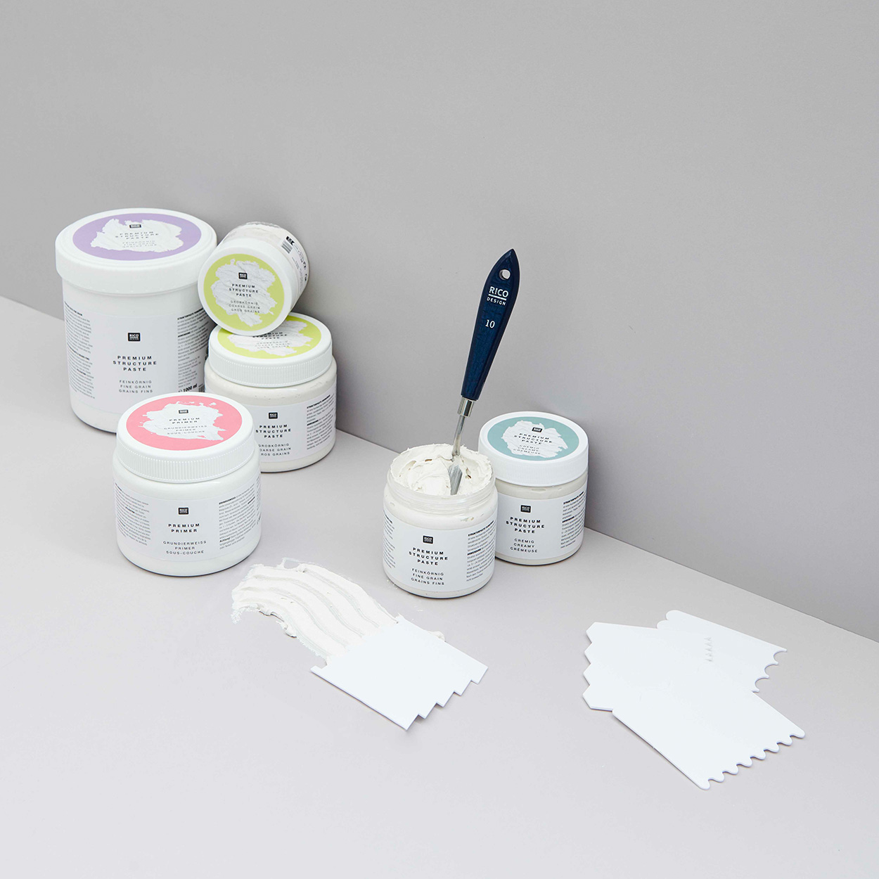 Strukturpaste in der Verpackung und mit Werkzeug. Fotosetting graue Ecke.