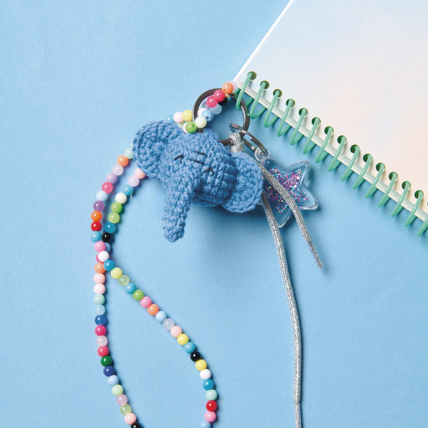 Ricorumi Rico Chingus Schlüsselanhänger in Elefantenform, gehäkelt in Blau, mit bunten Perlen und einem Sternanhänger auf blauem Hintergrund.