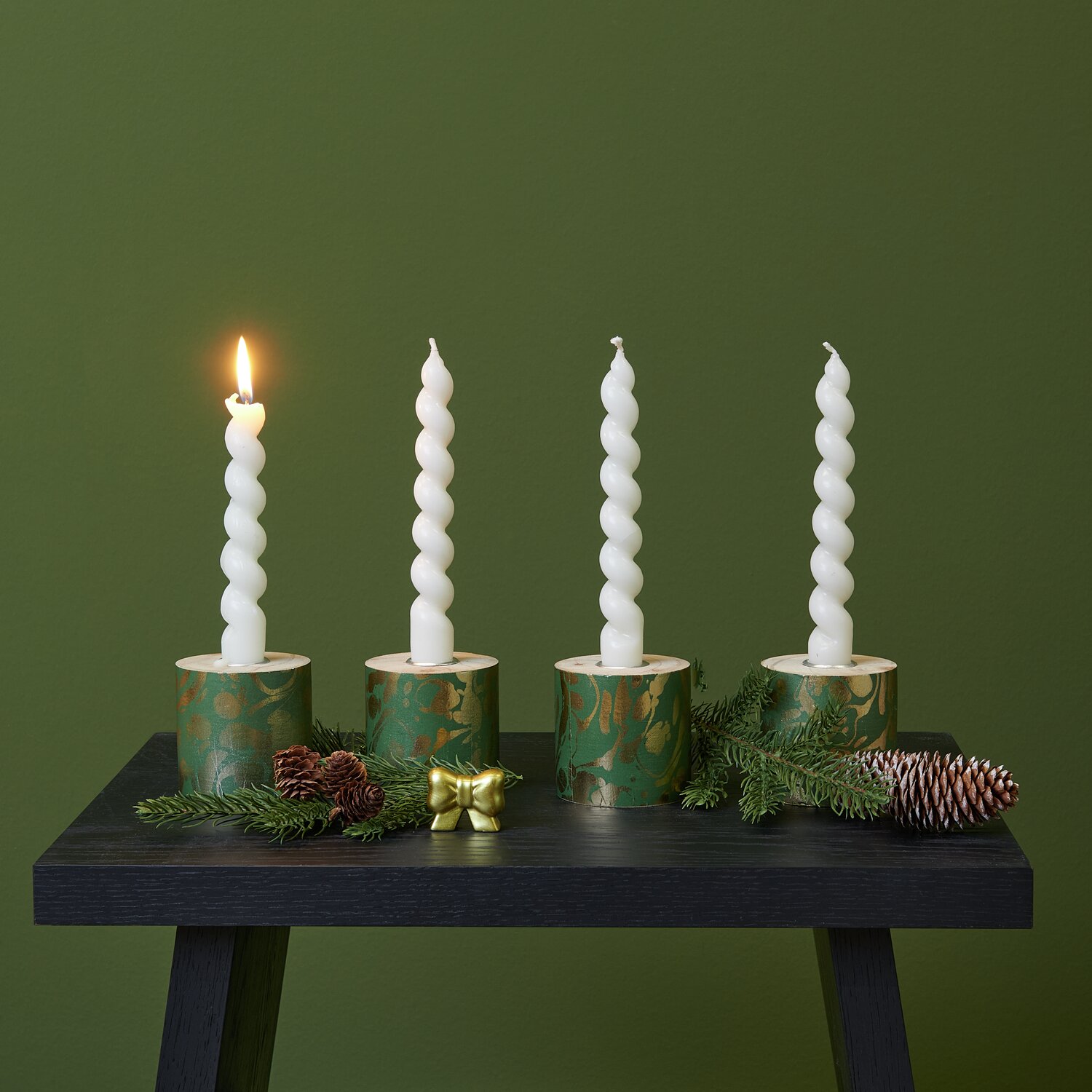 Paper Patch Weihnachtsmarkt marmoriert: Vier weiße Kerzen in grünen Haltern auf schwarzem Tisch.