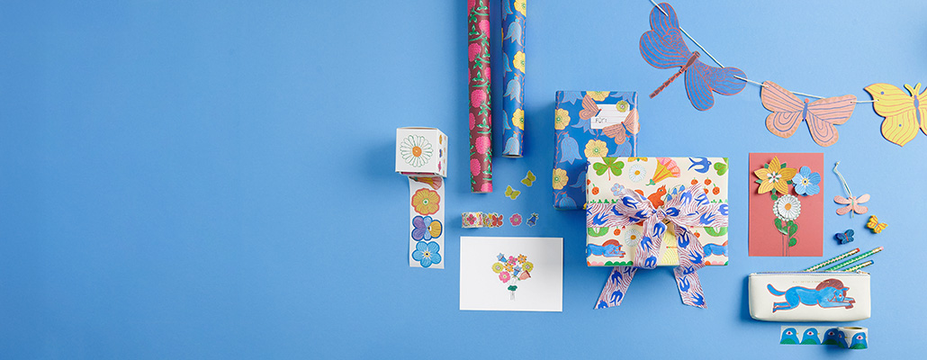 Geschenkpapier, eingepackte Geschenke, Blumensticker, Karten, Stifte in einem Etui und Girlande aus Schmetterlingen. Flatlay von Produkten.