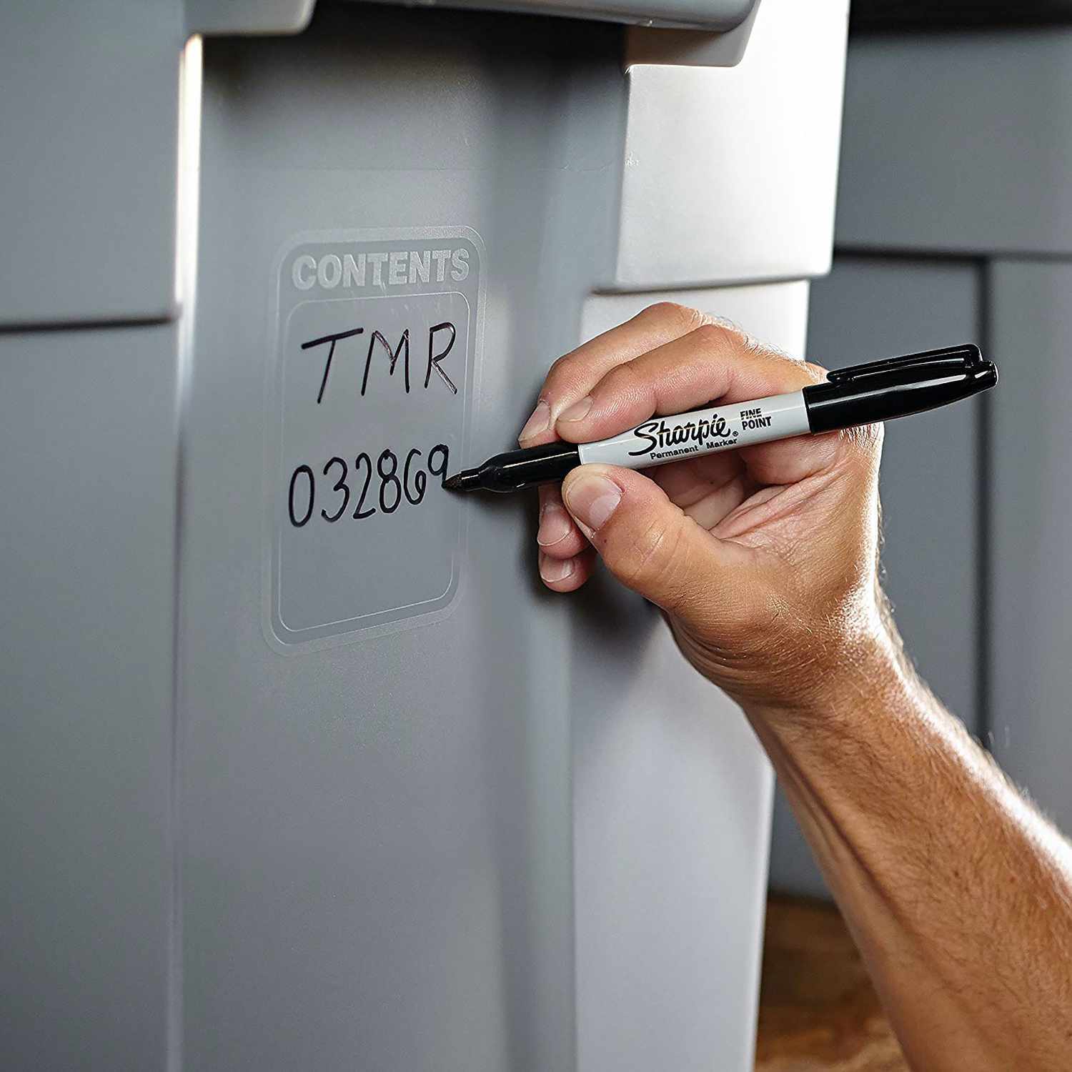 Permanentmarker 0,9mm: Eine Hand schreibt mit einem schwarzen Sharpie auf eine graue Kunststoffoberfläche.