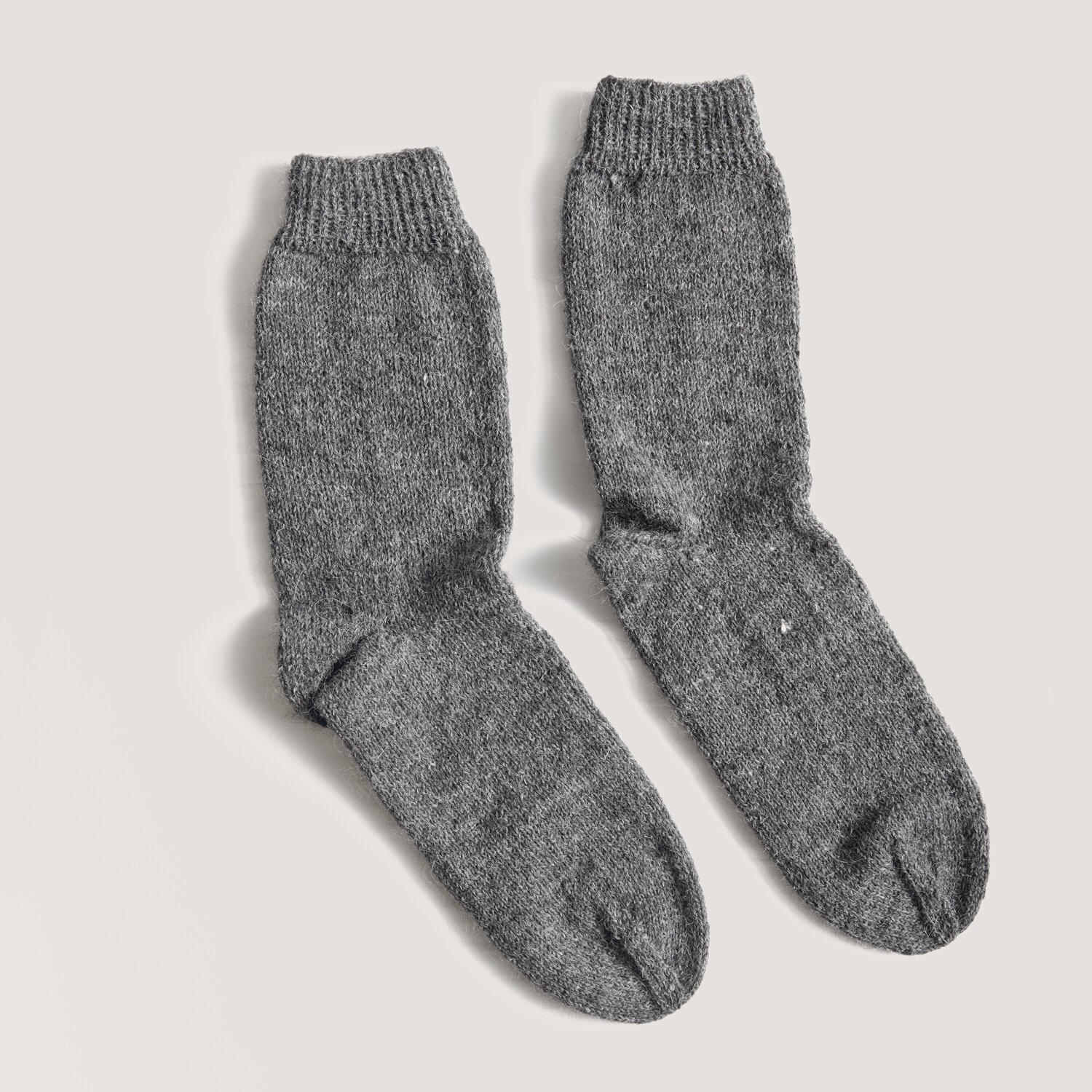 Luxury Merino Supercash dk 50g 160m Farbe Schwarz von Rico Design Made by Me Men No. 3 Socken aus grauer Wolle, gestrickt mit feiner Struktur, auf hellem Hintergrund.
