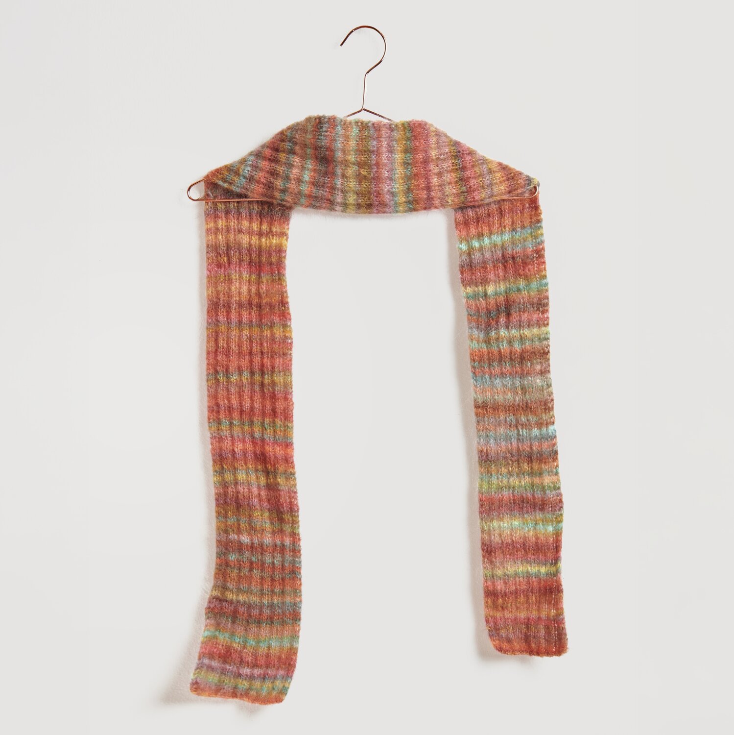 Die Neue Masche No. 13 Herbst von idee. Creativmarkt Strickset Schal Modell 10 aus Die Neue Masche No. 13 in bunten Herbsttönen auf einem Kleiderbügel. Fashion Meri Mohair Print verleiht weiche Textur.
