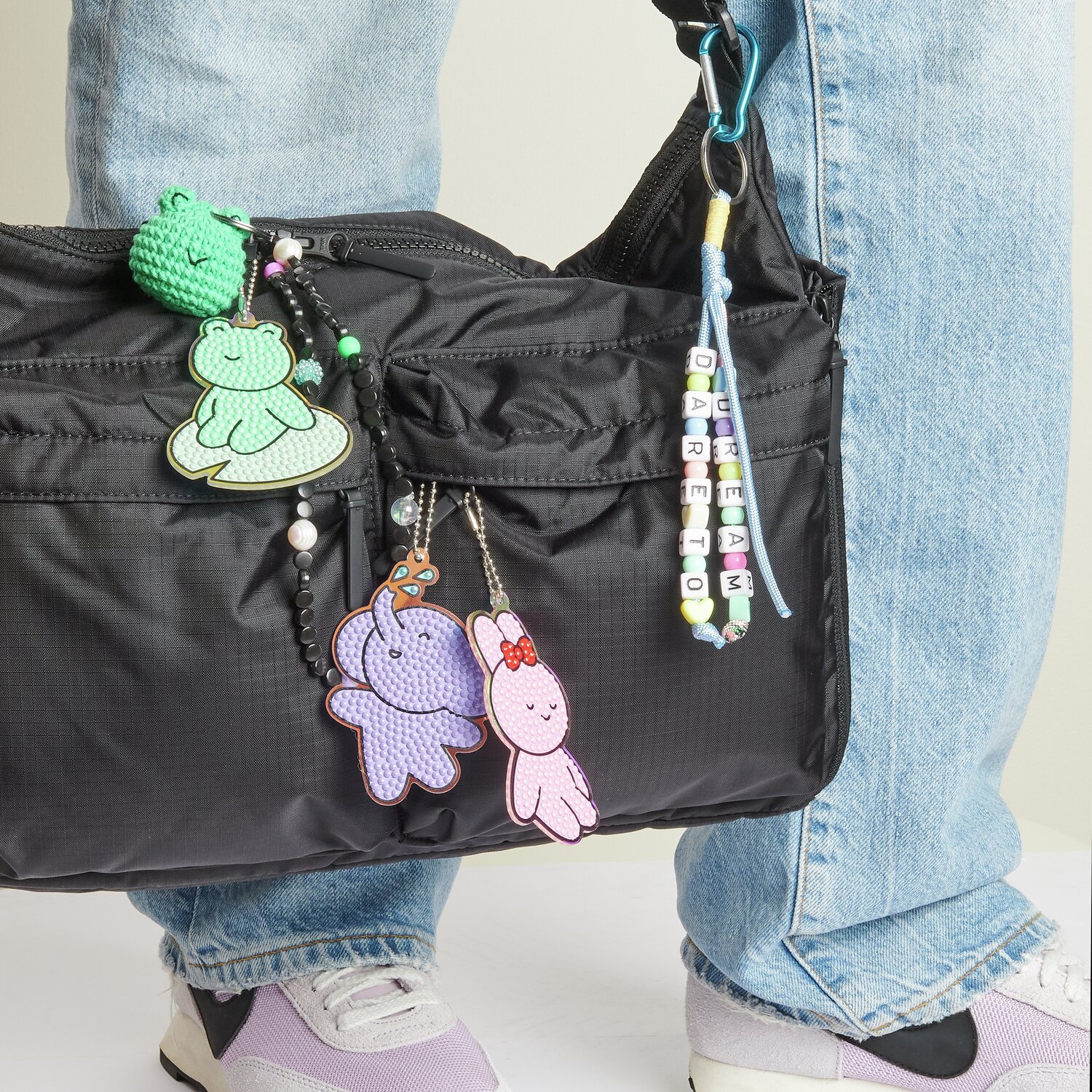 Diamond Painting Aufhänger Tiere an schwarzer Tasche mit bunten Anhängern und Jeans.