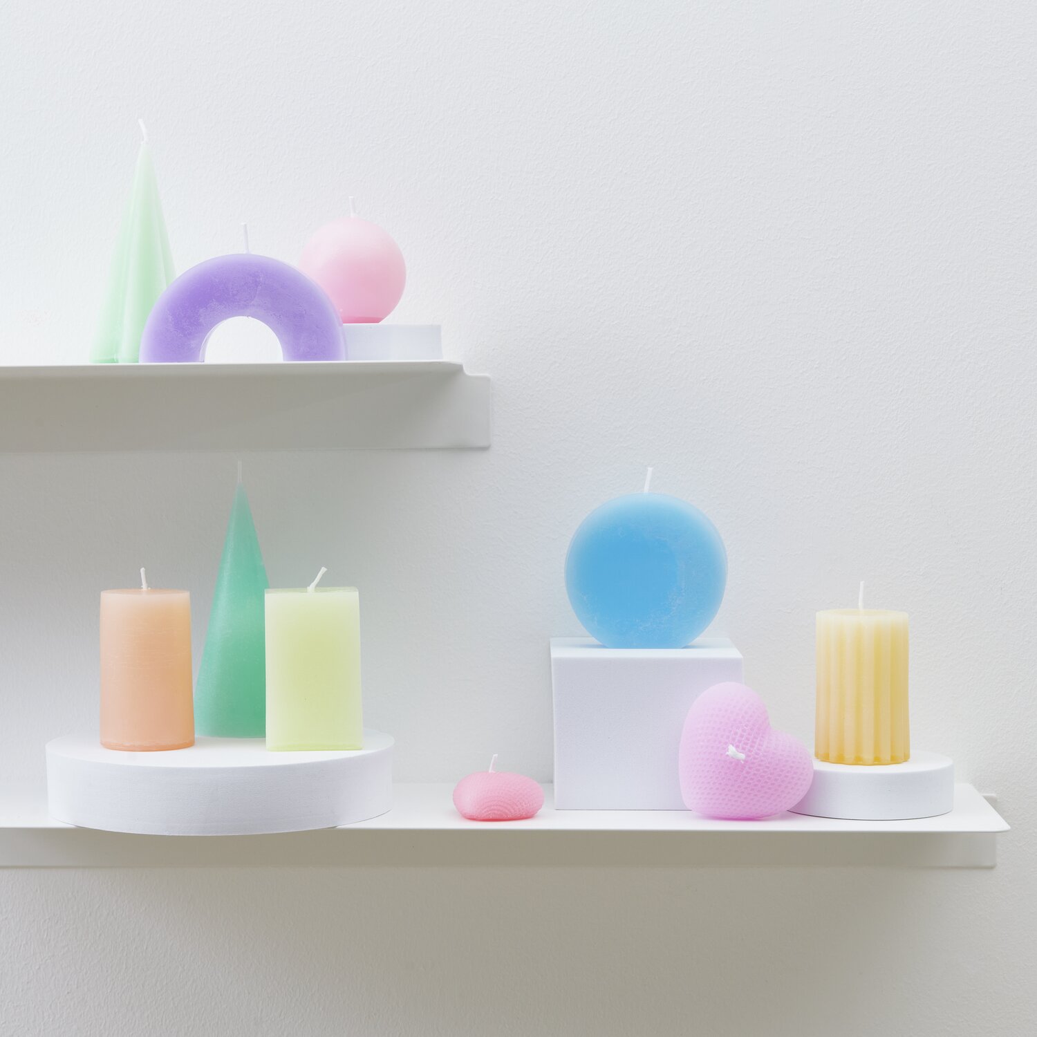 Kerzenwachs Granulat Größe 300g von Rico Design Kerzenwachs Granulat: Bunte Kerzen in Pastellfarben auf weißen Regalen, ideal für kreative Dekorationen.