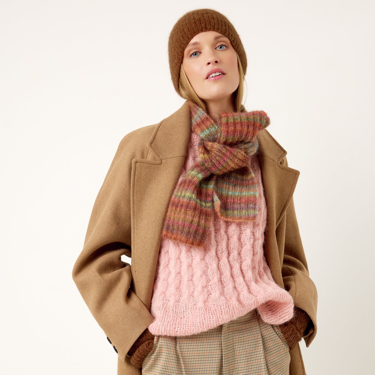 Strickset Schal Modell 10 aus Die Neue Masche No. 13 von idee. Creativmarkt Strickset Schal Modell 10 aus Die Neue Masche No. 13: Frau in beigem Mantel mit rosa Pullover und gestreiftem Schal.