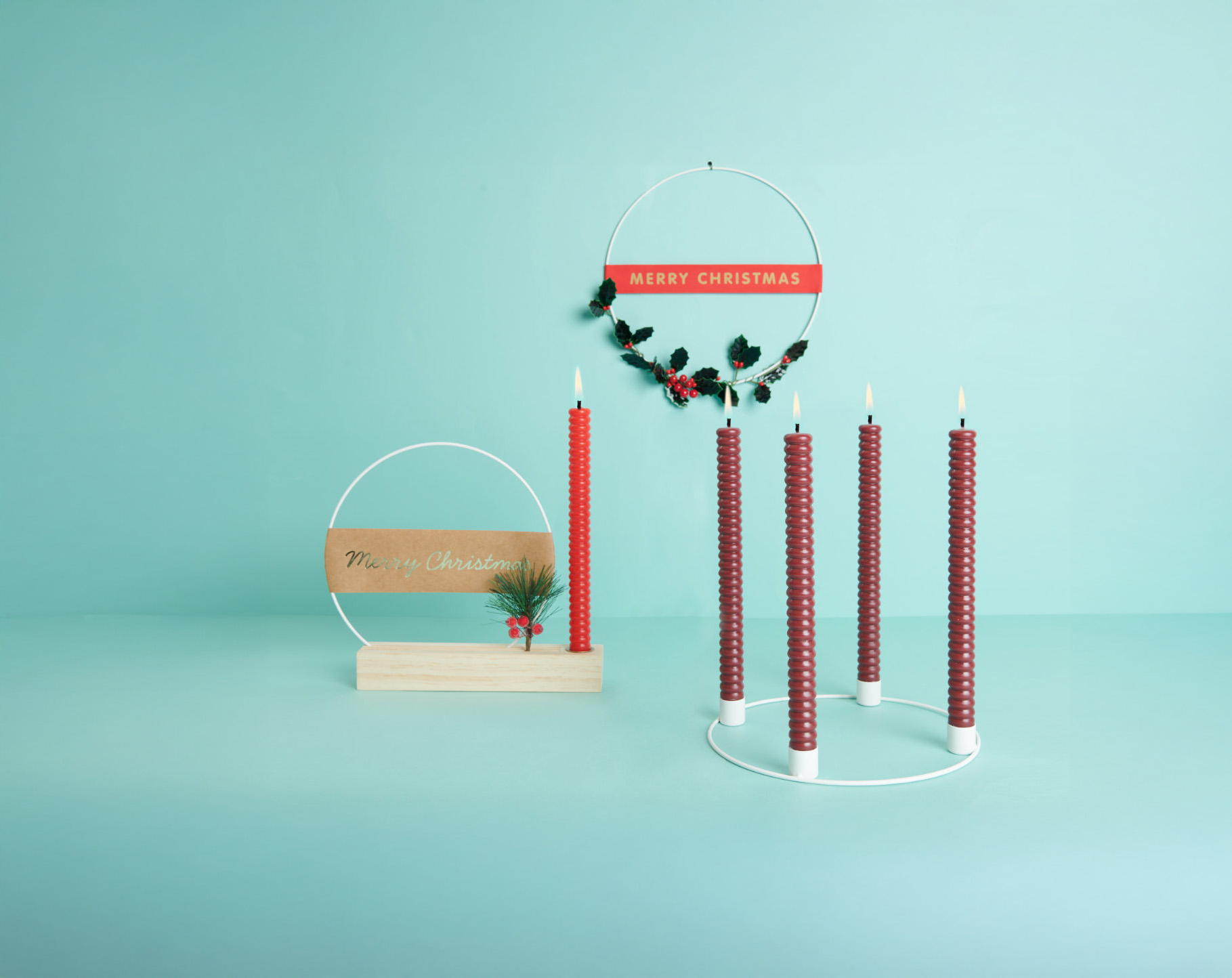 Ein hängender Dekoring mit Zweigen, ein Dekoring in einem Holzständer und ein Adventskranz-Dekoring mit vier roten Stabkerzen. Fotosetting türkise Wand.