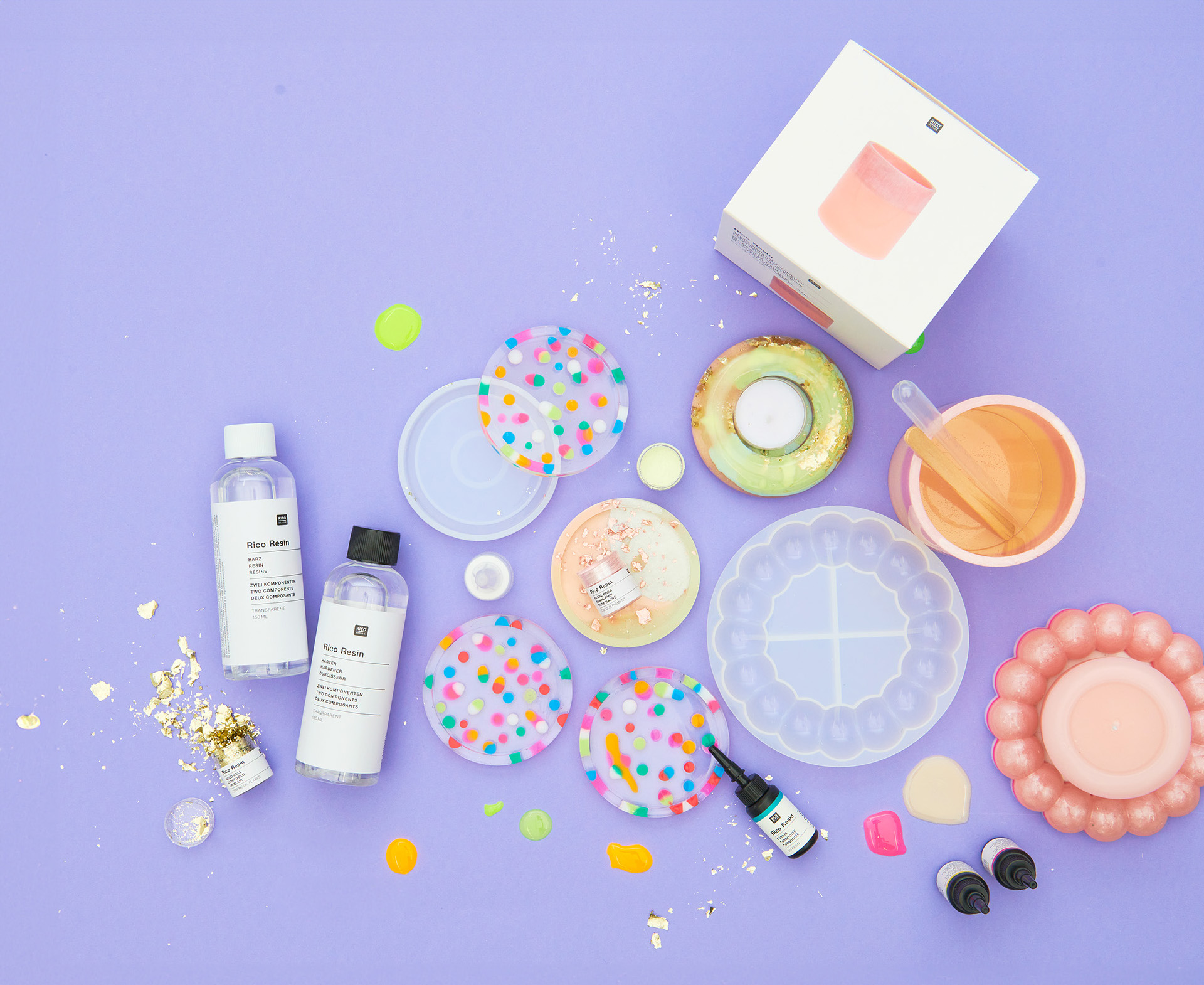 Flaschen mit buntem und transparentem Resin, Silikonformen, Farbpigmente und Blattmetall, sowie weiteres Zubehör zum Resin gießen und fertig gegossene Untersetzer. Flatlay von Produkten.