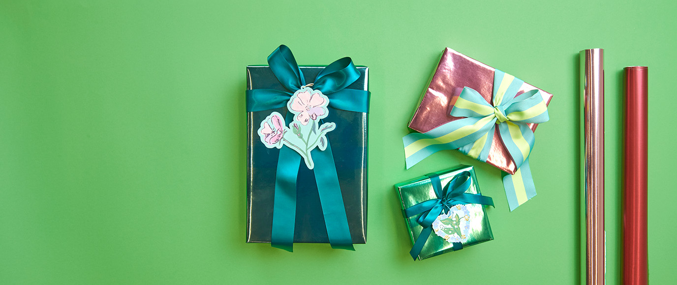 Drei Geschenke verpackt mit Geschenkpapier und Schleifenband sowie zwei Geschenkrollen