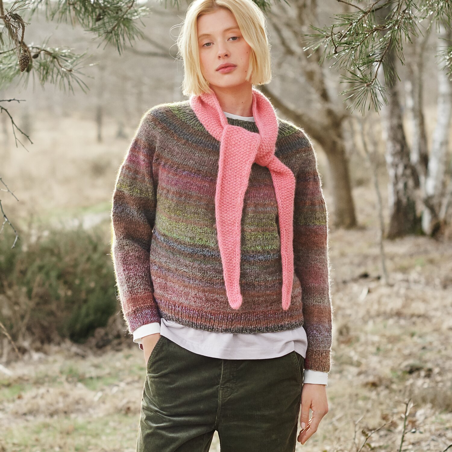 Strickset Minituch Modell 36 aus Lovewool No. 21 von Rico Design Strickset Pullover Modell 35 aus Lovewool No. 21: Frau im bunten Pullover mit rosa Schal im Wald.