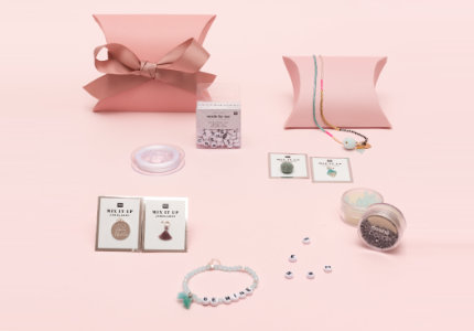 Mehrere pinke Geschenkschachteln mit Schmuckperlen, Schmuckband und verschiedenen Anhängern. Fotosetting rosa Wand.