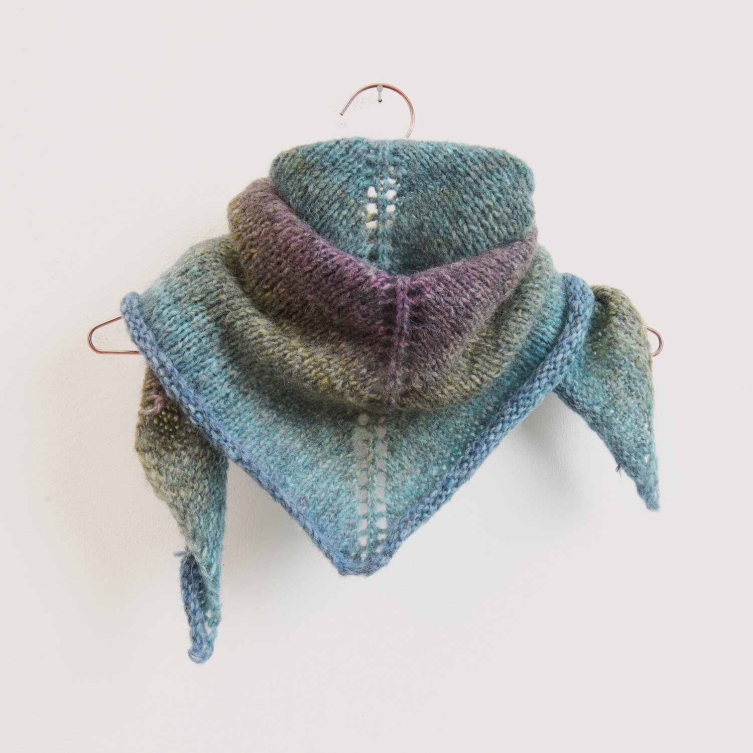 Die Neue Masche No. 16 Herbst, gestricktes Dreieckstuch von Wolle Rödel in melierten Blau- und Grüntönen, locker fallend auf Bügel vor hellem Hintergrund