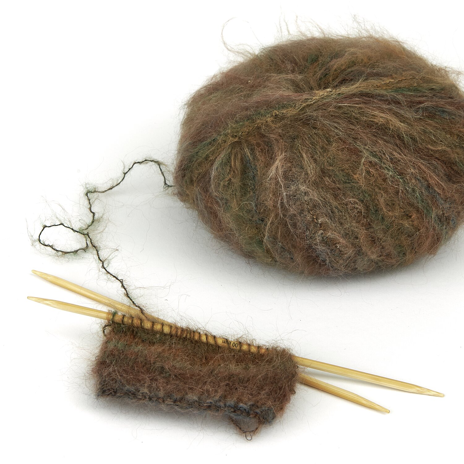Lovewool No. 21 Herbst-Winter Sprachauswahl deutsch von Rico Design Ein Knäuel braun-grünes Garn mit einem gestrickten Stück auf Holzstricknadeln. Perfekt für kreative Strickprojekte. Ideal für Handarbeitsliebhaber.