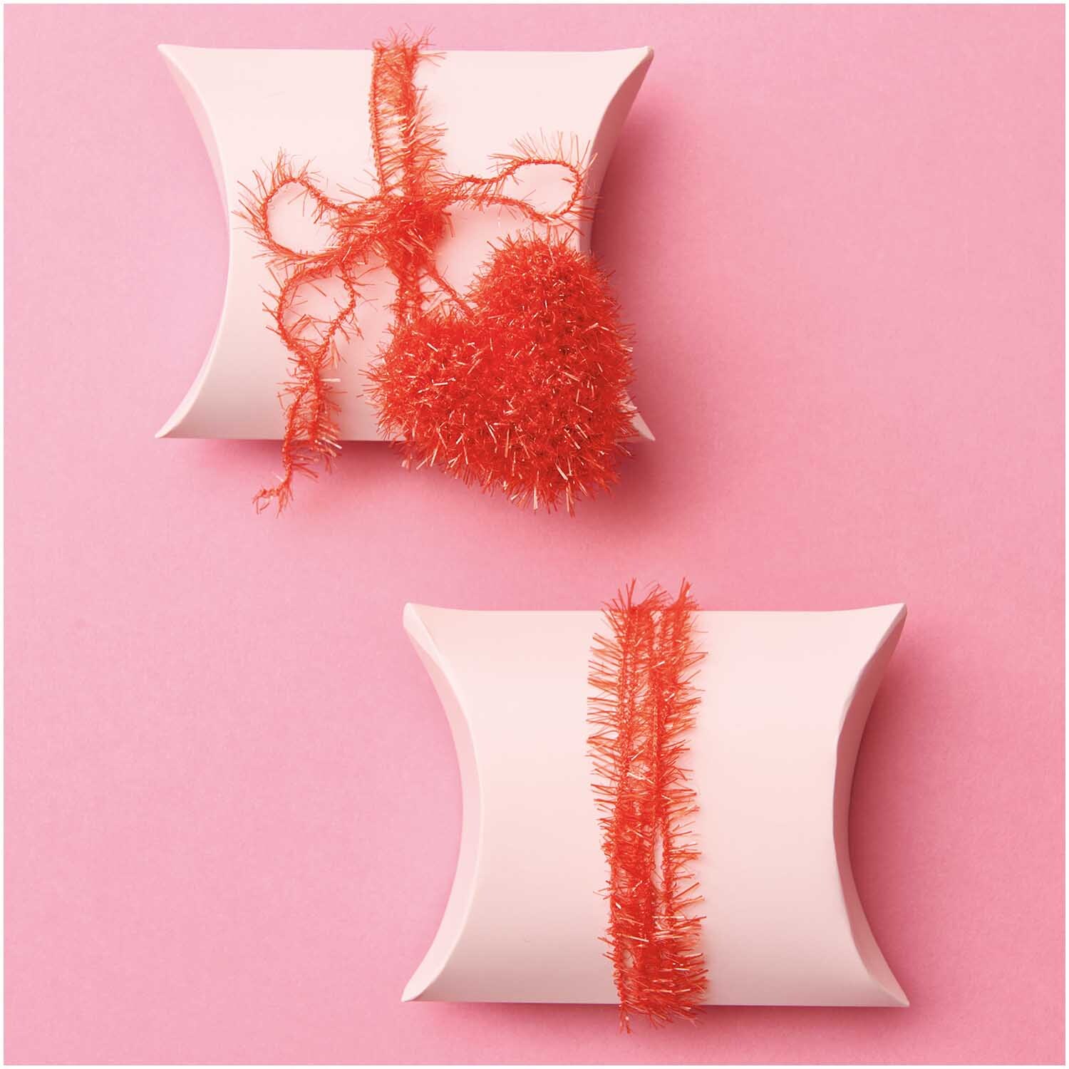 Creative Bubble: Zwei weiße Geschenkboxen mit rotem Garn von Rico Design auf rosa Hintergrund.