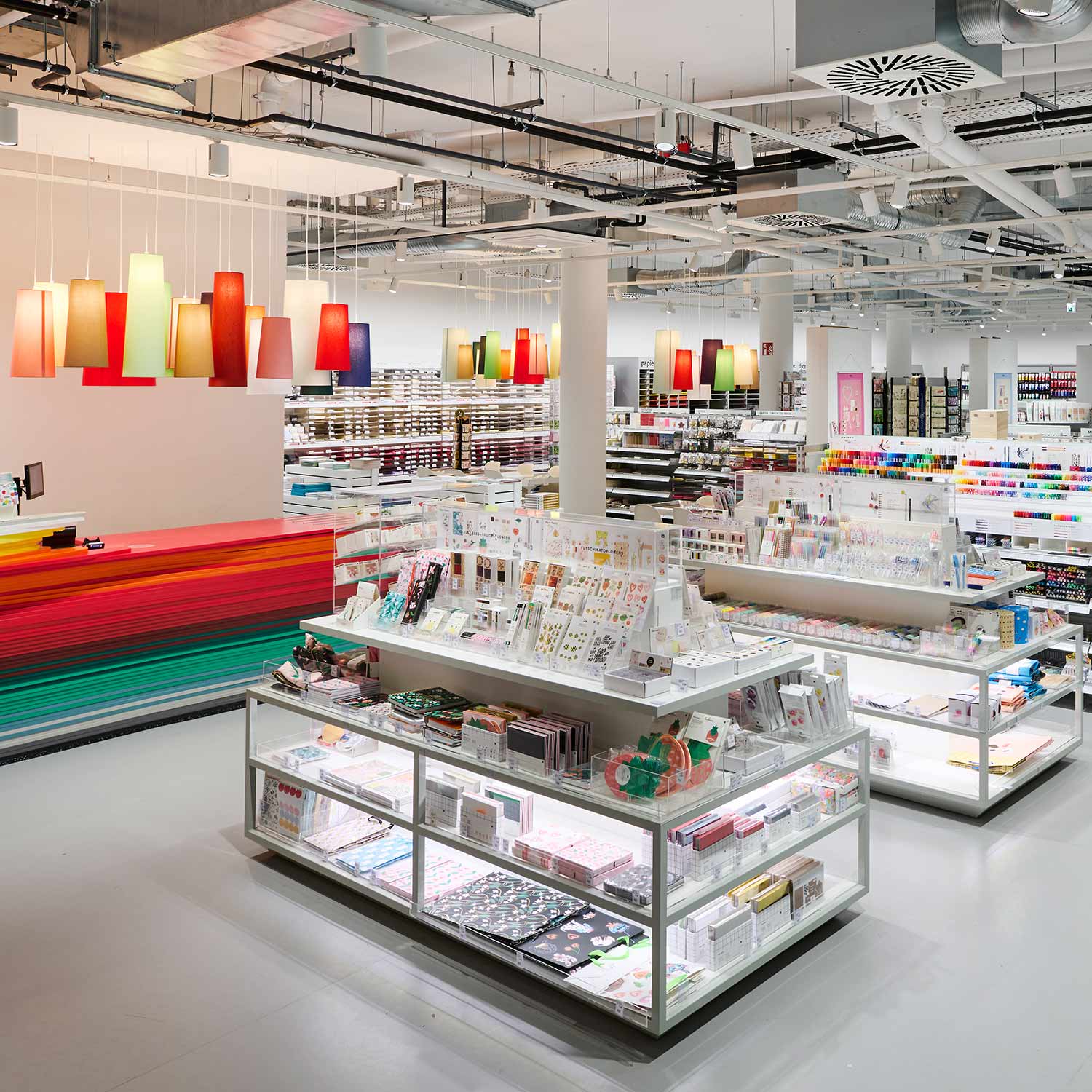 Eine idee. Creativmarkt Filiale von Innen fotografiert. Mehrere Tische und Regale mit buntem Papier und Schreibwaren, sowie eine regenbogenfarbene Kasse.