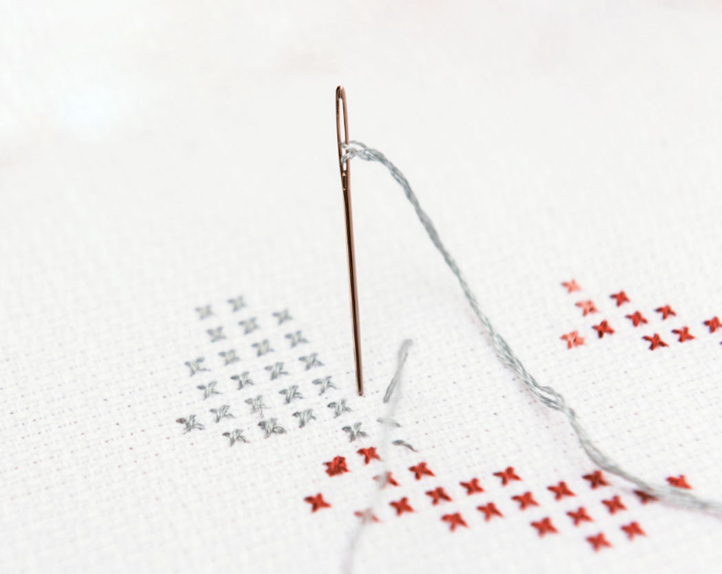 Nahaufnahme eines Stickring, welcher mit rotem und grauem Garn bestickt wird. 