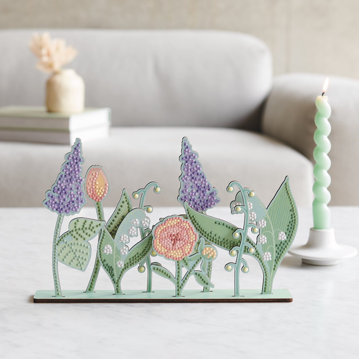 Diamond Painting DIY-Set Frühlingswiese zeigt bunte Blumen auf einem Tisch vor grauem Sofa.