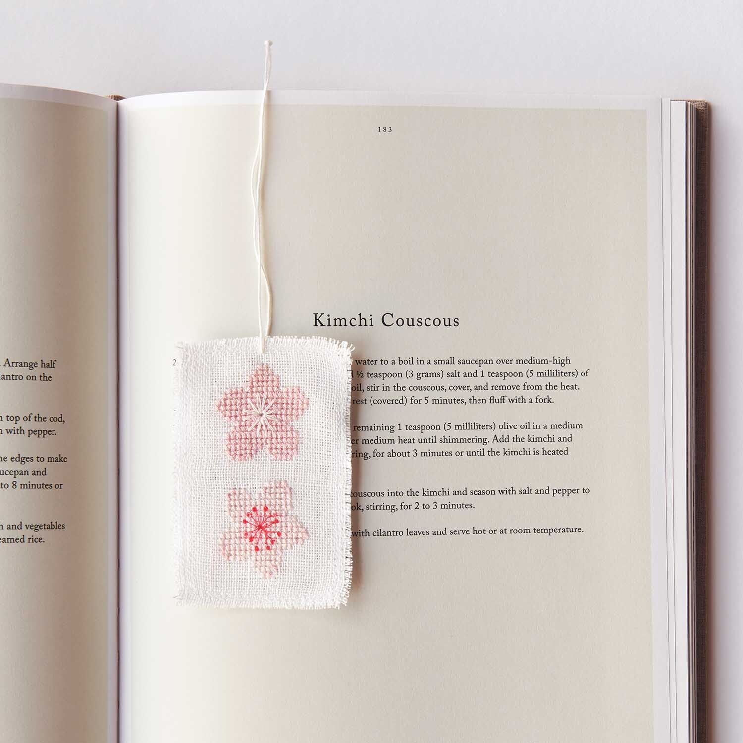 Stickanleitung Lesezeichen mit Kirschblüten: Weißes Lesezeichen mit rosa Blütenmotiv auf aufgeschlagenem Buch.