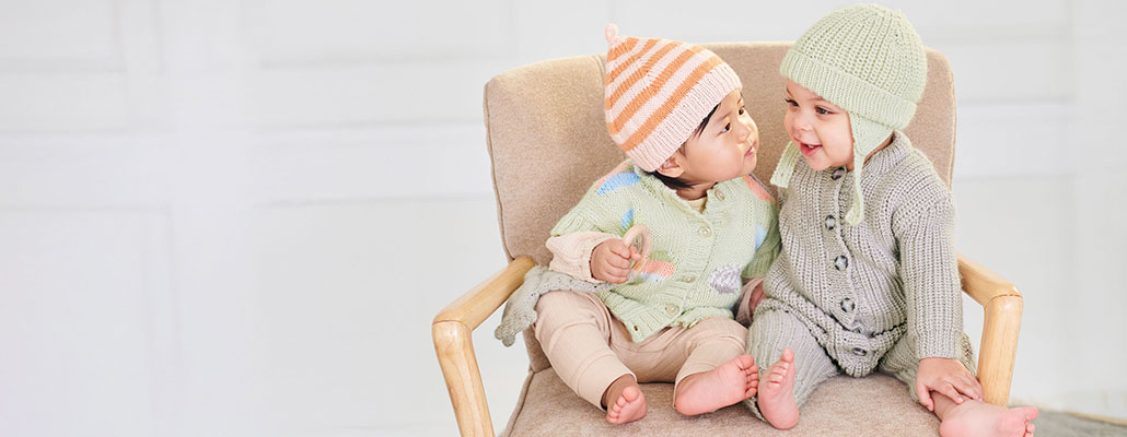 Baby in Strickjacken und Strickmützen sitzen auf einem Sessel