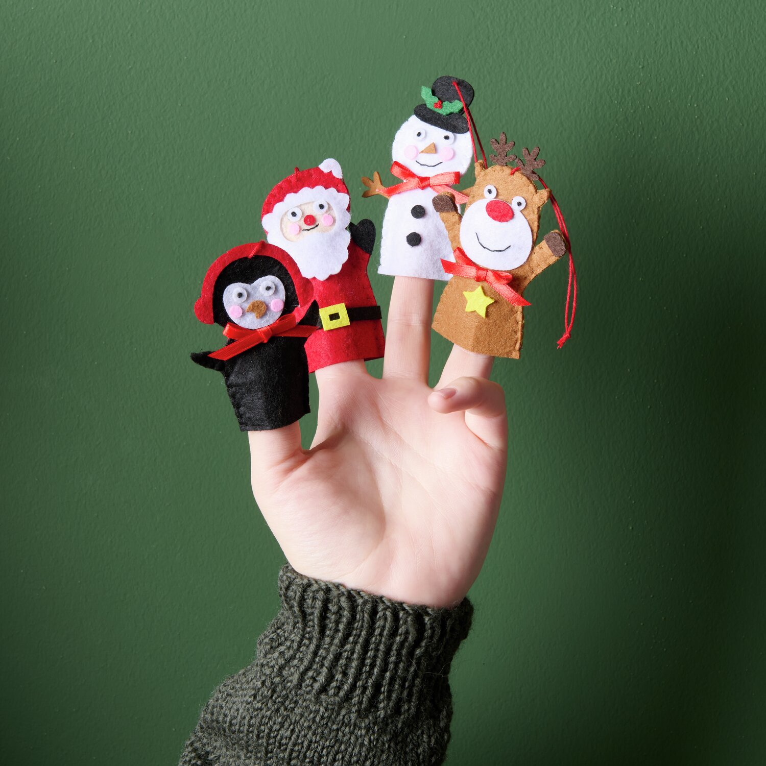 Aufhänger Filz-Rentier flach Braun, Weihnachtsmann, Pinguin und Schneemann als Fingerpuppen auf einer Hand vor grünem Hintergrund.