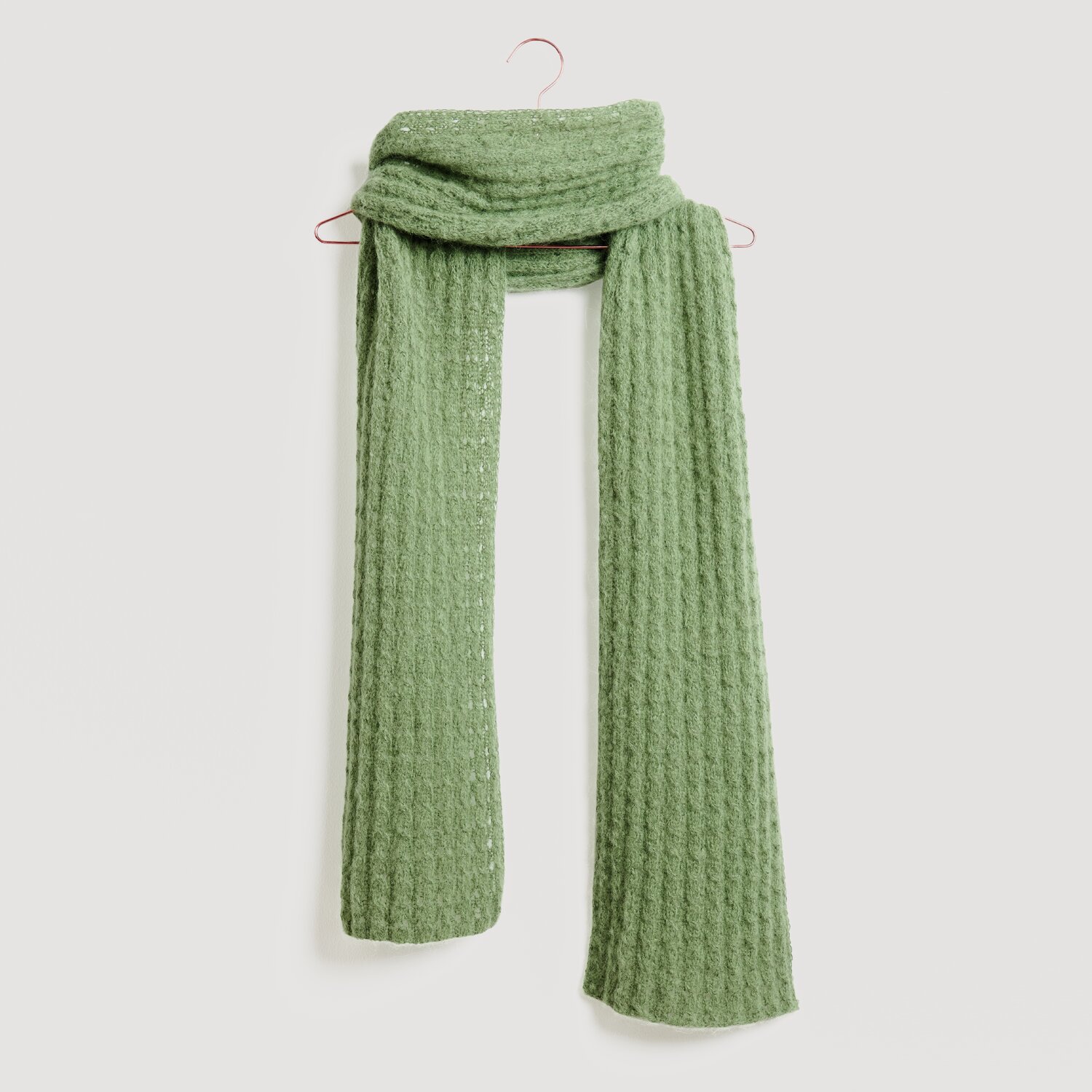 Lovewool No. 21 Herbst-Winter Sprachauswahl deutsch von Rico Design Grüner Schal von Modell Legeware, elegant drapiert auf einem Haken. Der Schal hat eine strukturierte Oberfläche und bietet stilvolle Wärme für kalte Tage. Ideal für modische Akzente.