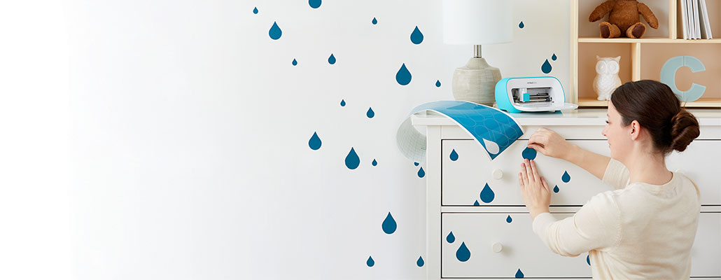 Frau beklebt eine Kommode mit Regentropfen, auf der Kommode steht ein Schneideplotter und Klebepapier.