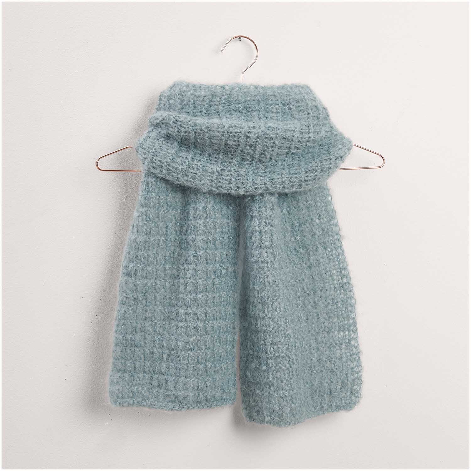 Weicher, hellblauer Schal aus dem Strickset Modell 21 von Made by Me Nr. 17. Der Schal hängt auf einem Kleiderbügel und zeigt ein feines, gestricktes Muster. Ideal für kühle Tage.