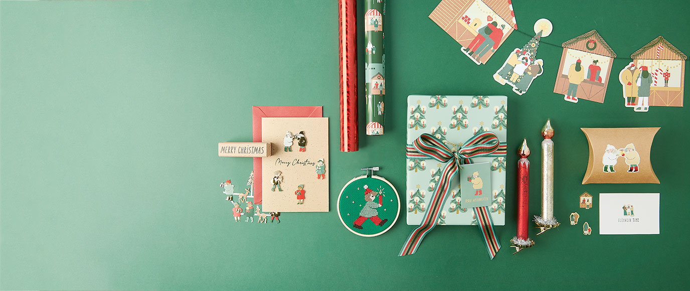 Ein verpacktes Geschenk, Geschenkpapierrollen, eine verzierte Weihnachtskarte, ein Stickring, eine verzierte Geschenkschachtel, Kerzen und eine Girlande alle in weihnachtlichem Stil. 