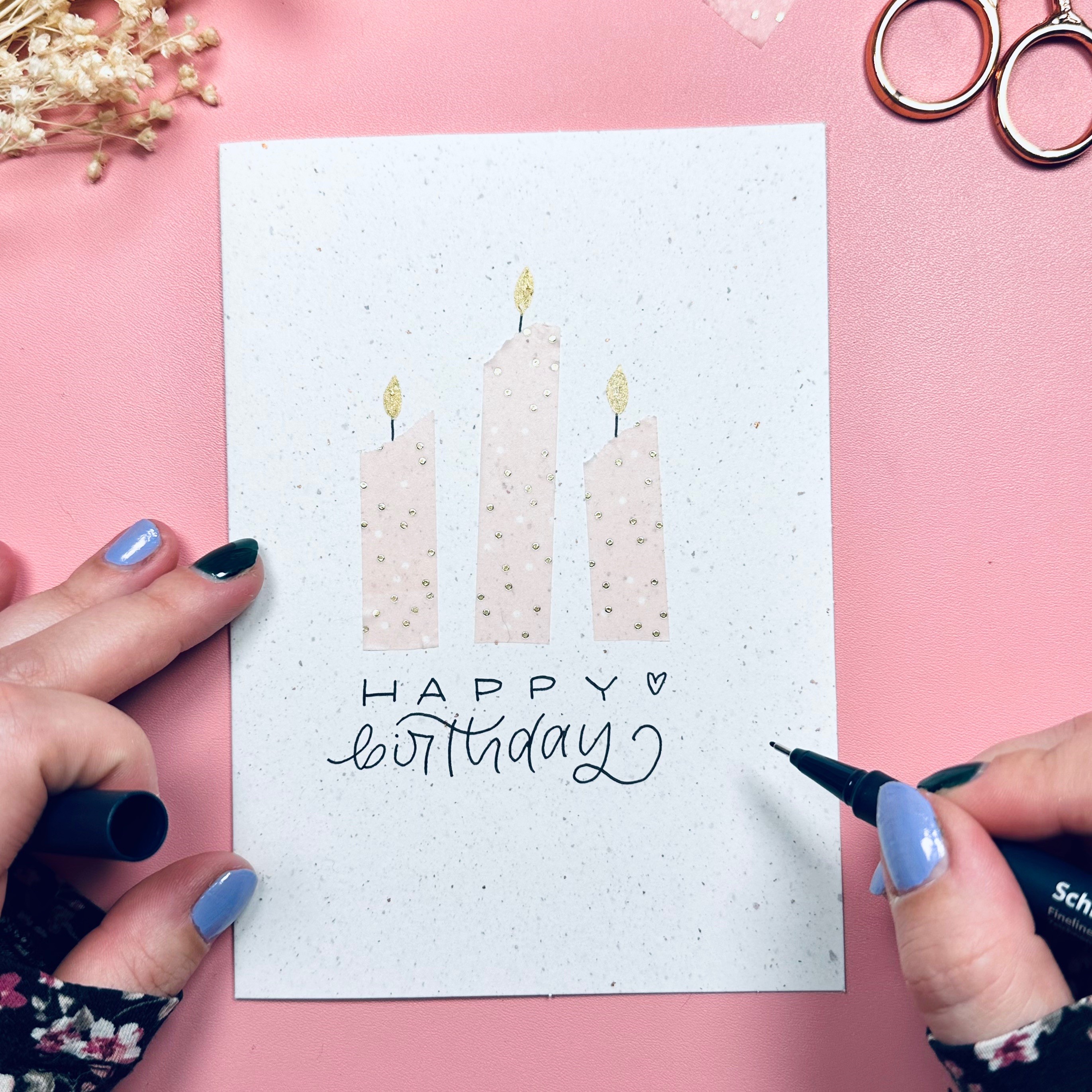 Eine Karte gestaltet mit drei Kerzen aus Washi-Tape und einem Schriftzug. Hände welche einen Stift zum Beschriften der Karte halten.
