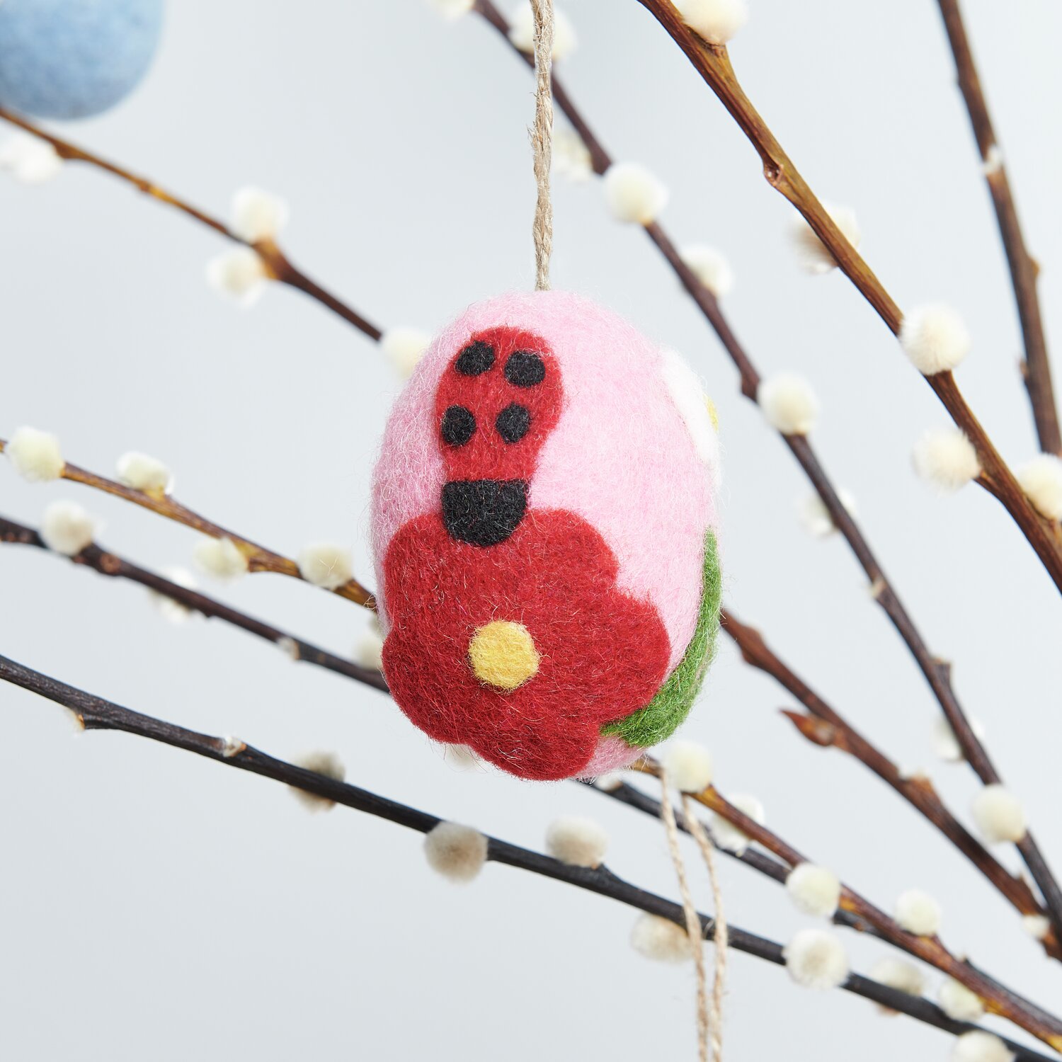 Aufhänger Filz-Ei Marienkäfer: Rosa Filz-Ei mit rotem Marienkäfer und Blume, dekorativ an Zweig.