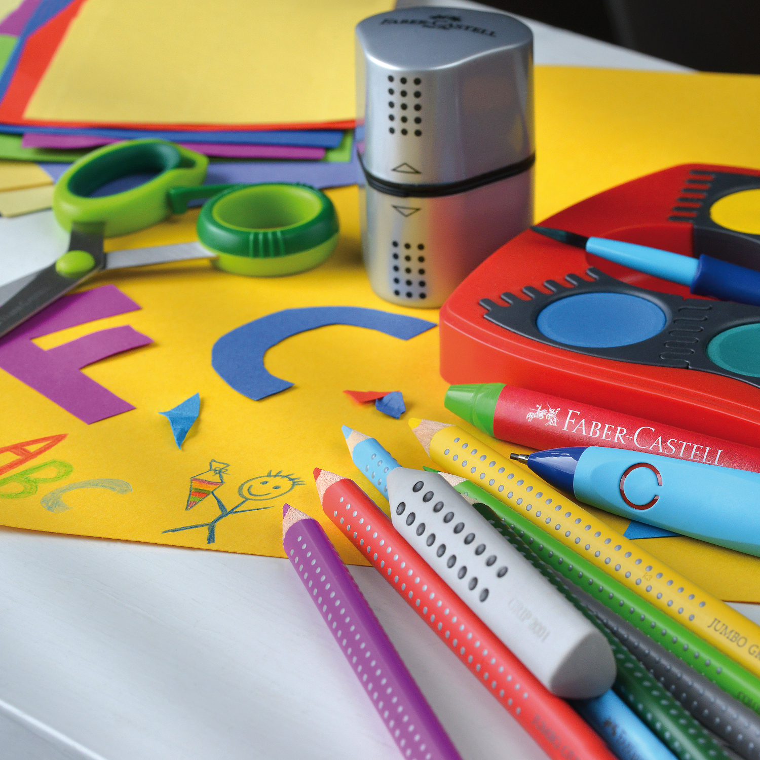 Jumbo Grip Farbstift von Faber Castell in einer kreativen Szene mit Schere, Anspitzer und buntem Papier.