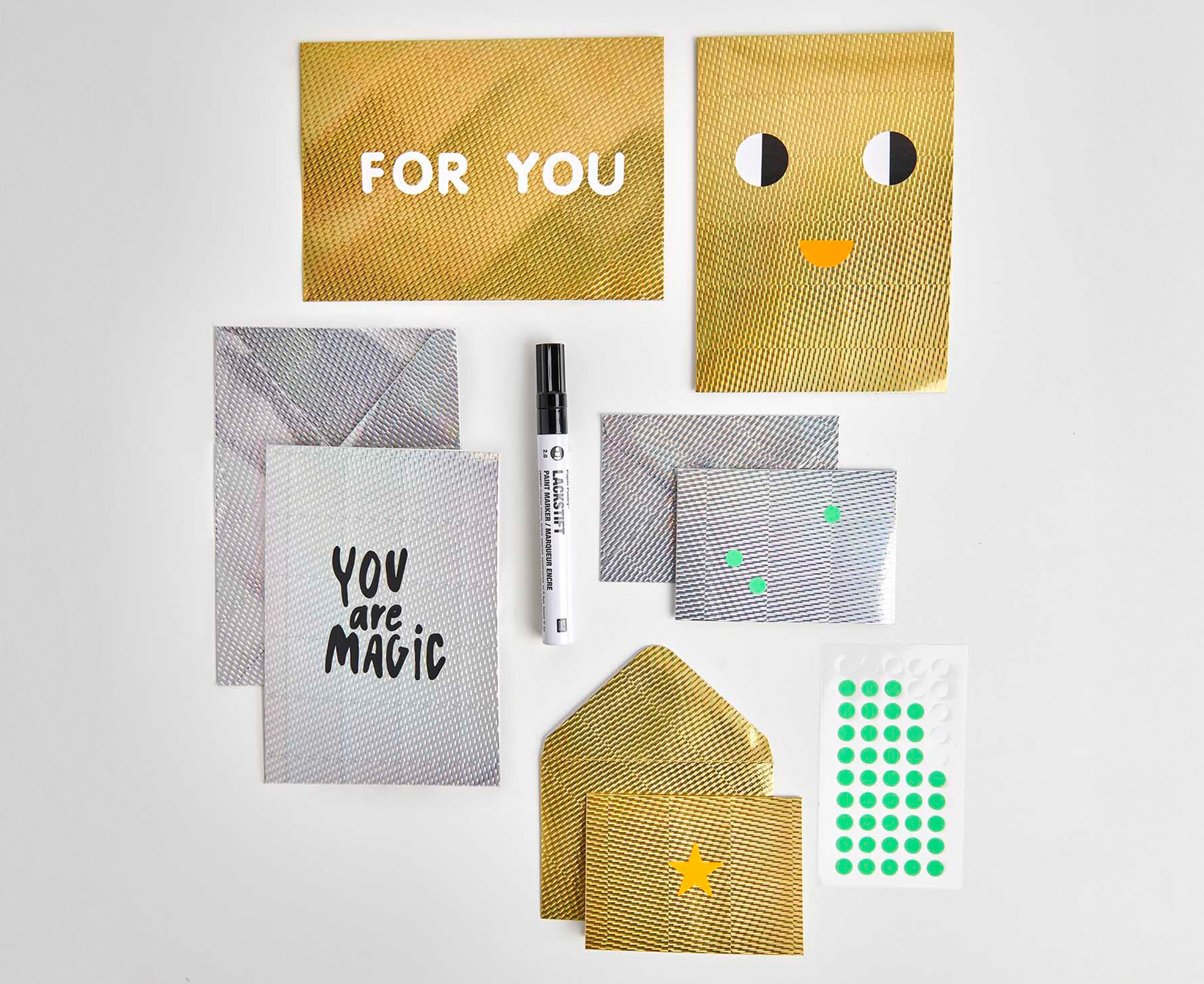 Nebeneinander platzierte silberne, goldene Karten und Umschlag aus Effektpapier, mit Schrift und Stickern gestaltet. Flatlay von Produkten.
