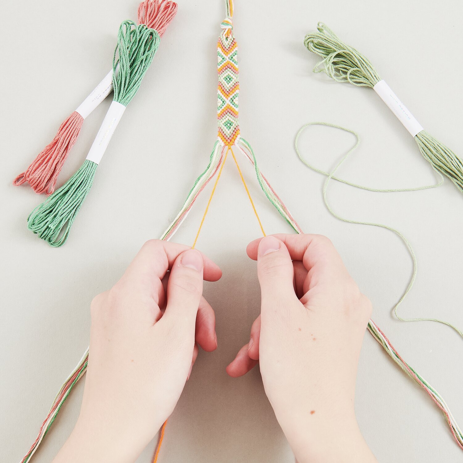DIY Freundschaftsarmbänder Set Neon Mix Colours: Hände flechten bunte Armbänder mit Garn in Pastelltönen.
