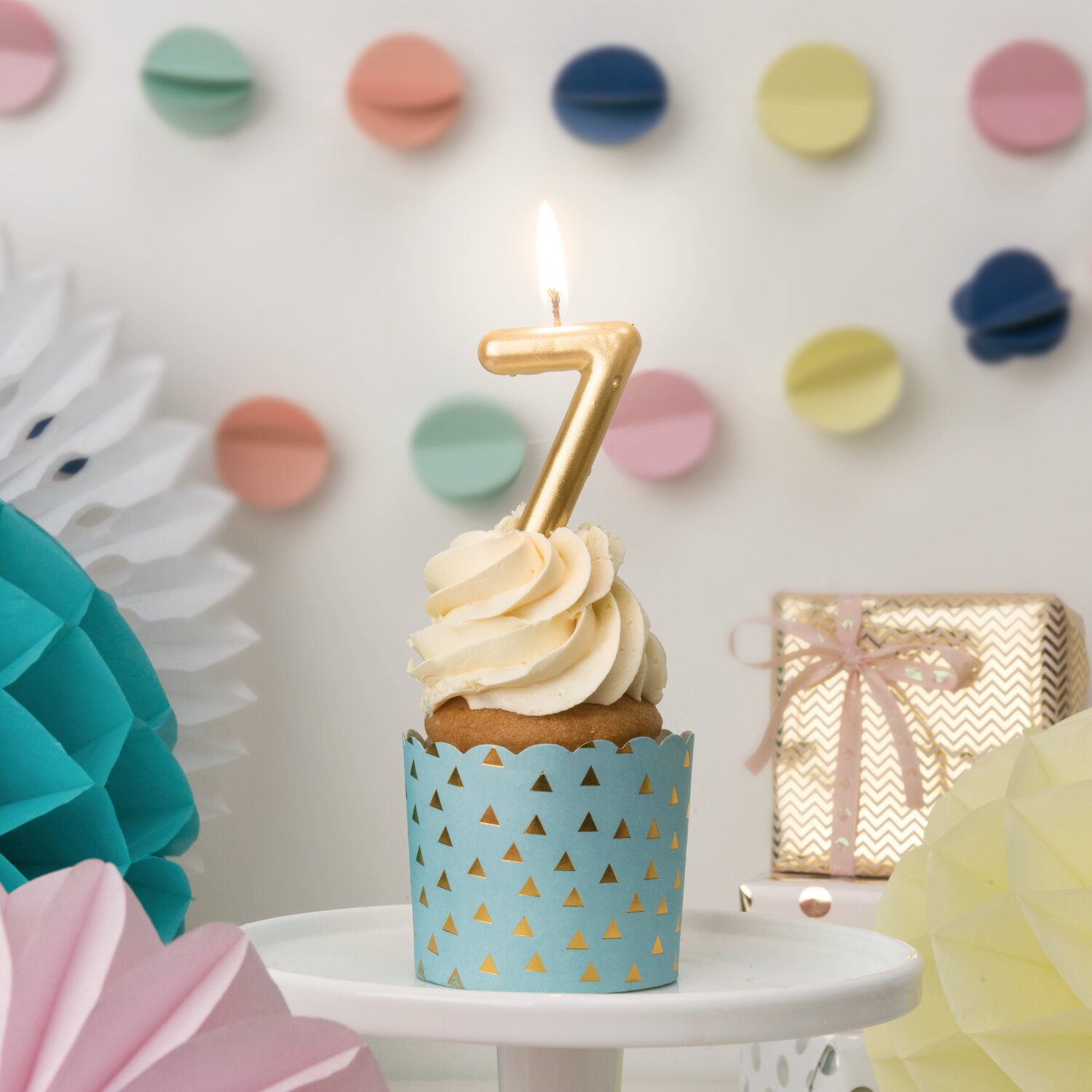 Zahlenkerze Gold auf Cupcake mit Cremehaube, Rico Design Deko, im Hintergrund bunte Papiergirlande und Geschenk für festliche Geburtstagstafel