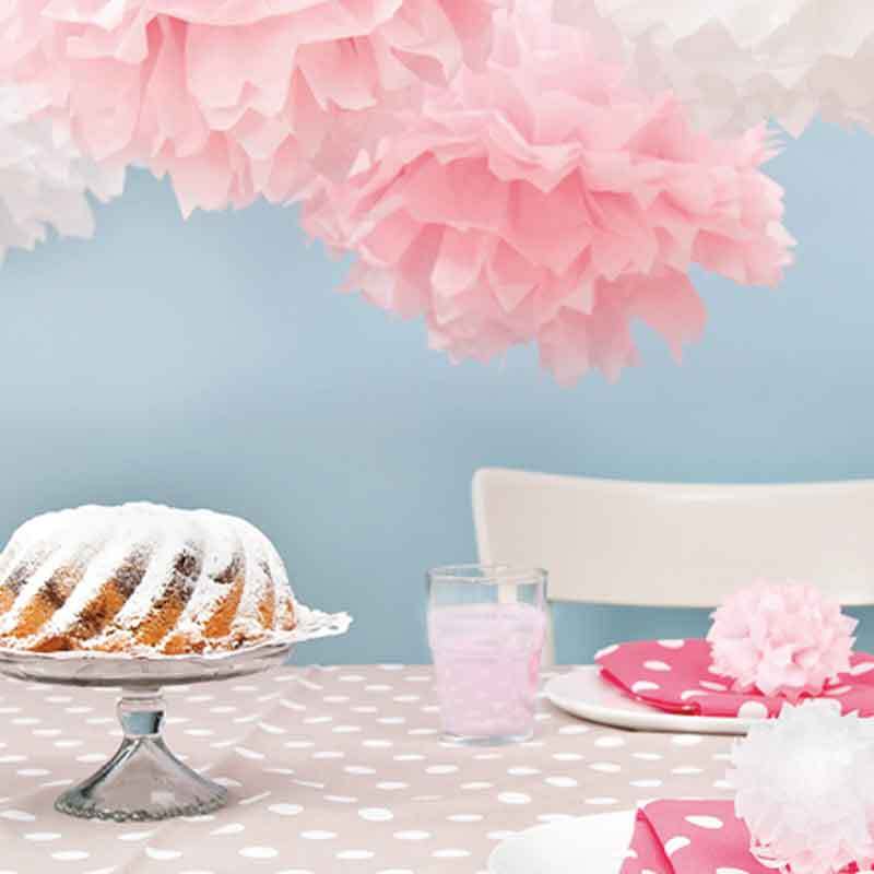 Seidenpapier 50x70cm 5 Bogen von Rico Design dekoriert einen Tisch mit rosa und weißen Pompons, einem Kuchen und einem gepunkteten Tischtuch.