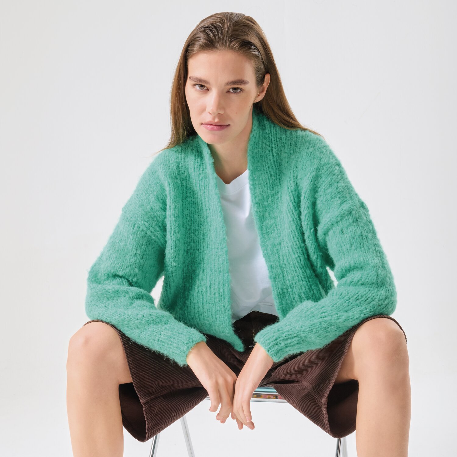 Strickset Jacke Modell 17 aus Made by Me No. 21 von Rico Design Strickset Jacke Modell 17 aus Made by Me No. 21: Weiche, grüne Strickjacke, lässig getragen von einer Person auf einem Stuhl sitzend.
